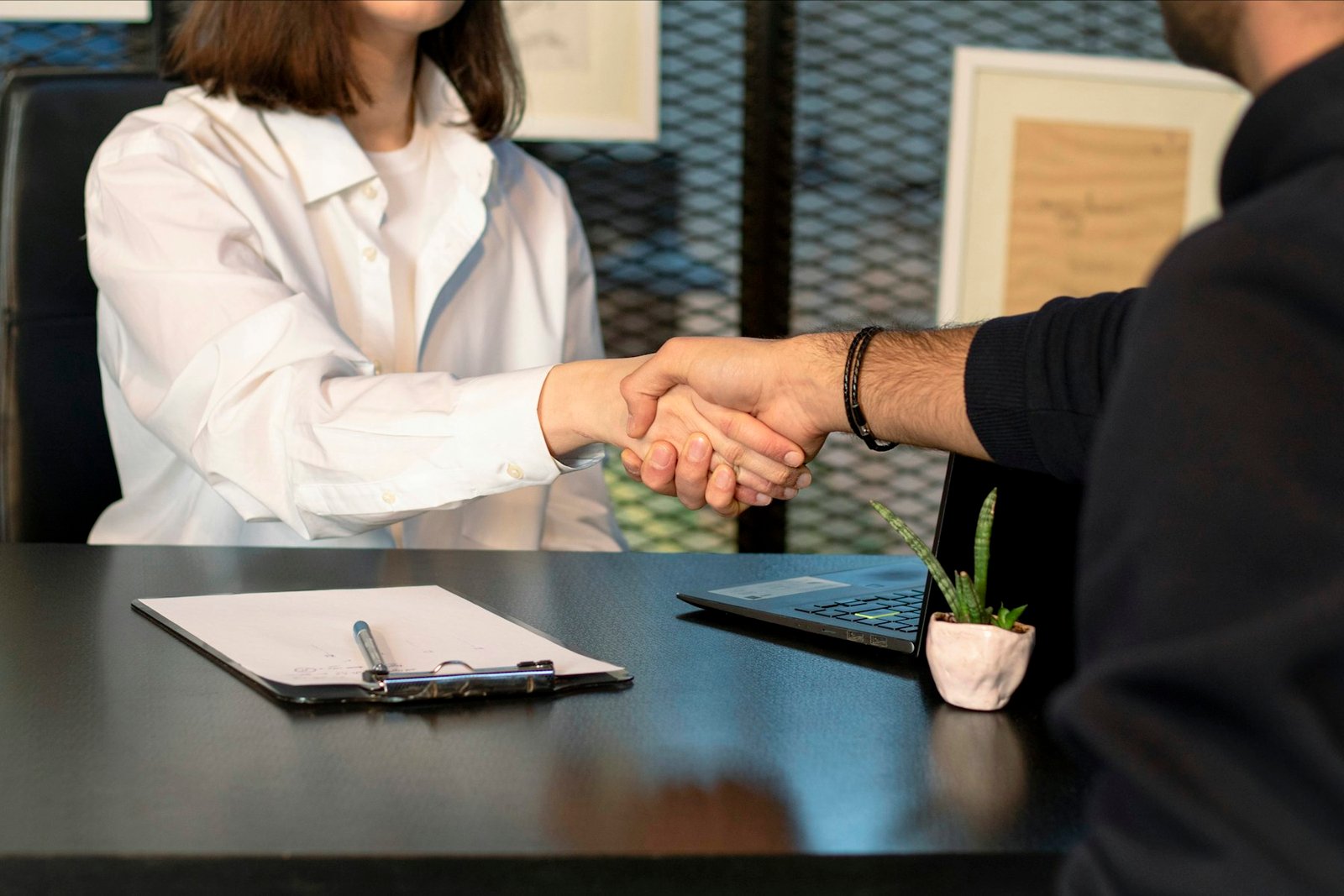 A woman and a man shaking hands across a desk — agreement on terms.